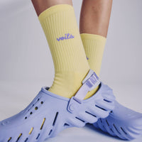 Person wearing yellow socks with 'Voila' branding and blue clogs on a light gray background